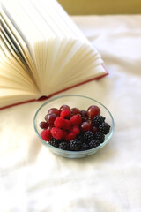 Bowl of raspberries, blackberries and grapes with open book. Selective focus.