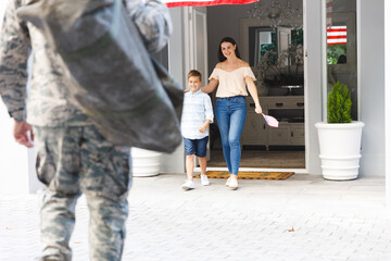 Caucasian male soldier with son and wife outside house decorated with american flag