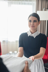 cheerful chambermaid giving towels to blurred colleague