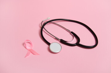 Phonendoscope and satin pink ribbon awareness, International symbol of Breast Cancer Awareness Month in October. Isolated on pink background with copy space .Women's health care and medical concept.