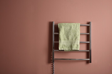 Modern heated towel rail with warm soft towel on pink wall. Space for text