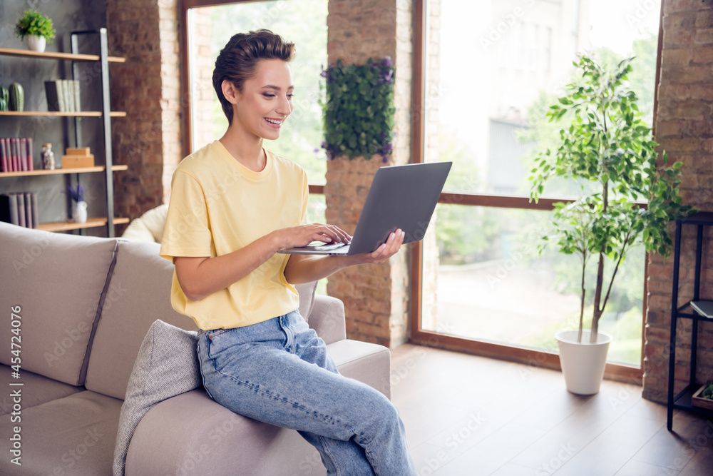 Poster Photo of pretty sweet young lady wear yellow t-shirt sitting sofa typing modern gadget indoors room home