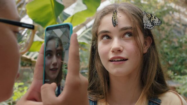 beautiful butterflies on girls face with happy friend taking photo using smartphone friends having fun in zoo wildlife sanctuary sharing excursion on social media 4k footage