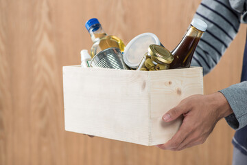 Volunteer with donation box with food stuffs on wooden background