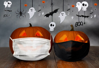 holidays, halloween and health concept - carved pumpkins or jack-o-lanterns in medical masks on wooden table over garland on grey gloomy background