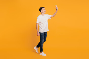 Fototapeta na wymiar Portrait of positive handsome guy take selfie hold phone walk on yellow background