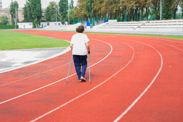 Fototapeta premium An elderly woman is engaged in walking with sticks in the stadium.