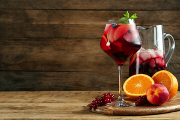 Glass and jug of Red Sangria with fruits on wooden table, space for text