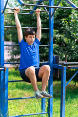 Fototapeta na wymiar teenage boy exercising outdoors, sports ground in the yard, he hangs on the horizontal bar, raises his legs and shakes his abs, healthy lifestyle
