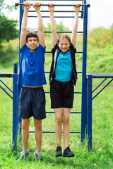 Obraz premium teenage boy and girl exercising outdoors, sports ground in the yard, they posing at the horizontal bar, healthy lifestyle