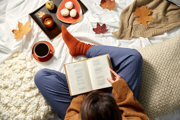 people, season and leisure concept - young woman reading book at home in autumn