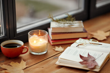 season, leisure and objects concept - open book, cup of coffee, autumn leaves and candle on window sill at home