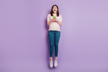Portrait of funky carefree energetic lady hold cellphone jump have fun on violet background