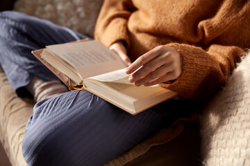 people, season and leisure concept - close up of woman in warm sweater reading book at home - obrazy, fototapety, plakaty