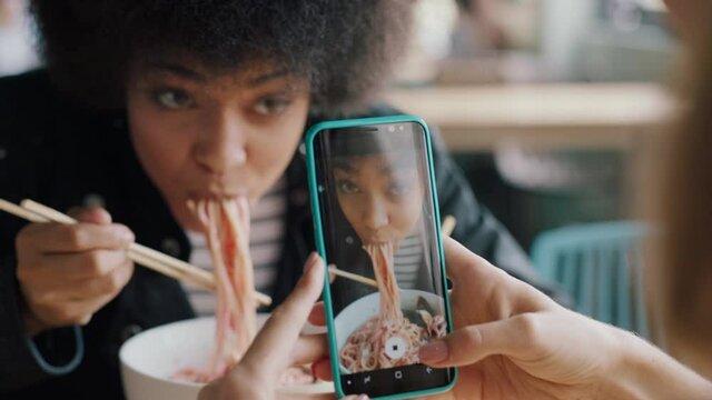 beautiful african american woman eating spaghetti at restaurant with friend using smartphone taking photo having fun sharing weekend together on social media 4k
