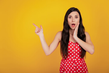 Portrait of crazy woman finger show up empty space open mouth palm cheek wear dotted red dress on yellow background