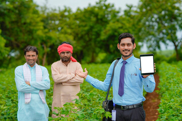 Young indian agronomist or banker showing tablet with farmers at agriculture field.