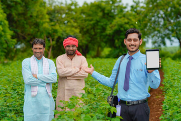 Young indian agronomist or banker showing tablet with farmers at agriculture field.