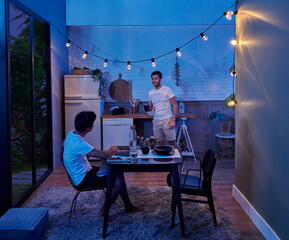 Two men living together at the same home, they are having dinner, modern room night concept, kitchen and sitting room style.