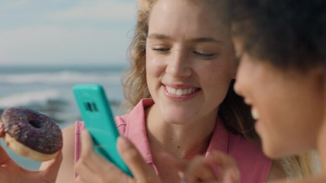 two young women friends looking at photos on smartphone enjoying sunny day on beach 4k footage