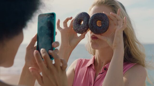 beautiful woman posing with donuts on beach best friend taking photos using smartphone sharing weekend by seaside on social media enjoying summertime fun 4k