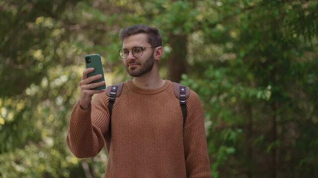 One male tourist with a backpack with a mobile phone in a forest area takes a video, photographs natural views. Creation of video content, online broadcast.