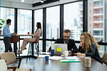 Businessman and businesswoman working laptop computer and tablet in the office with city blur background