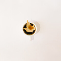 cup of coffee with yellow gold autumn leaf in the middle.white background nature minimal art concept