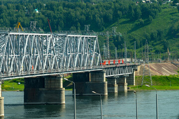 An electric train travels across a railway bridge across a river in an industrial city.