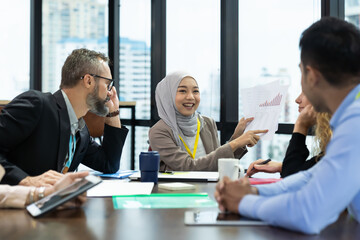 Asian Muslim business woman in hijab headscarf sitting on wheelchair presenting of her work to corporate colleagues in meeting in the modern office. diverse corporate colleagues and multicultural