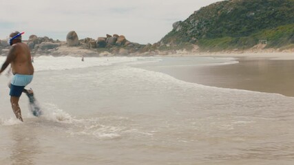 funny african american man walking on beach in sea water wearing flippers getting ready to swim enjoying summer by ocean 4k