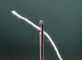 Thread white is threaded through eye of needle, close-up macro view