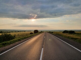 The paved road goes into perspective at sunset, among nature.