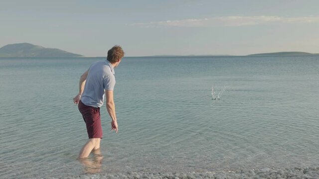 Slow motion - Young adult caucasian man skipping stone on water