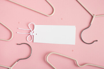 Empty tag card with clothes hangers on pastel pink background. Sale, discounts and shopping...