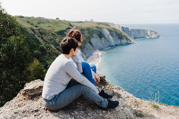 Fototapeta na wymiar two women friends sitting and looking at beautiful sea landscape on top of the mountain. Friendship and nature concept