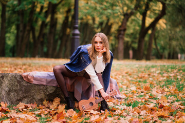 Beautiful woman playing ukulele guitar at outdoor in autumn forest