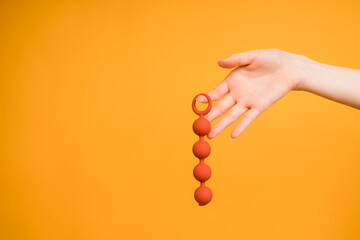 A woman's hand holds red Kegel balls on an orange background.Useful for a sex shop