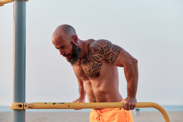 Strong athletic man exercising during calisthenic workout outdoors at the beach.