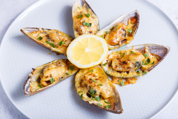 Baked Greenshell mussels in half a shell with cheese, parsley and lemon on a white plate....