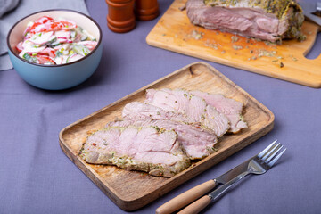 Roasted turkey thigh on a wooden board, cut into pieces. In the background is a bowl of vegetable salad and a turkey. Close-up.