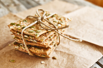 Crunchy crispbread on recycled paper on wooden table. Whole Grain crisp bread with pumpkin, sunflower, chia, linen and sesame seeds. Healthy snack. Bio-organic dieting product.