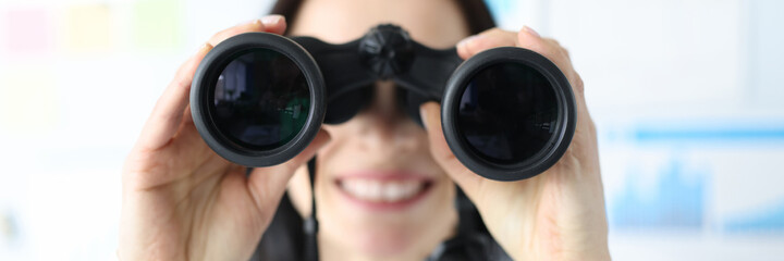 Woman looking in black professional binoculars in office closeup