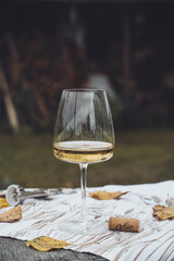 Autumn picnic in nature with white wine. There is a glass on a cloth napkin, next to a cork from an open wine and yellow leaves. There is firewood in the background. autumn mood.