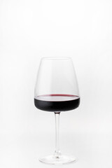 A glass of red wine stands on a white background. Droplets of condensation are visible on the glass. Cold red wine. Space for the text. An alcoholic drink.