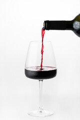 A glass of red wine stands on a white background. From the bottle, wine is poured into a glass. Droplets of condensation are visible on the glass.Space for the text.  An alcoholic drink.  Wine tasting