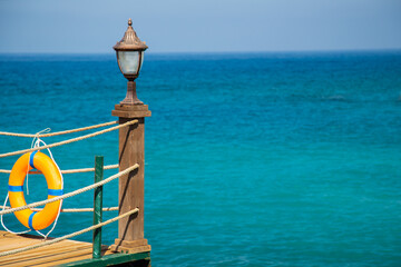 Wooden pier with lantern and orange lifebuoy. Sea background