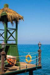 Rescue tower with lifebuoy and life jacket on a wooden pier. Sea background