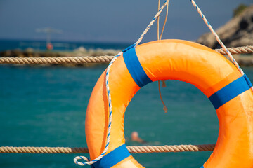 Orange lifebuoy near the rope fence on a pier. Close up. Sea background