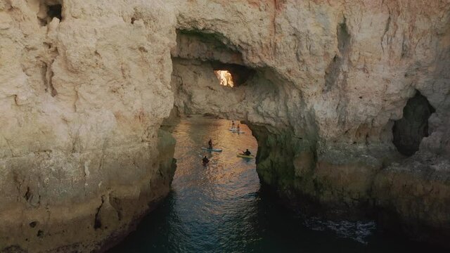 Drone view of people on paddleboards floating in cave of Ponta de Piedade, Portugal, Lagos, Europe. Women and men exploring mountains from the water. Panoramic shot of amazing landscape, 4k footage